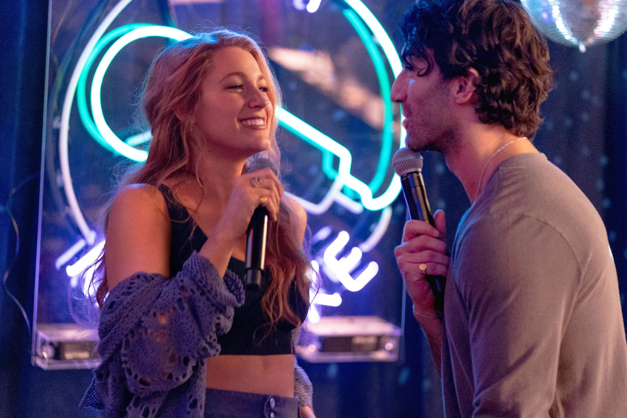 Blake Lively and Justin Baldoni holding microphones in It Ends With Us.