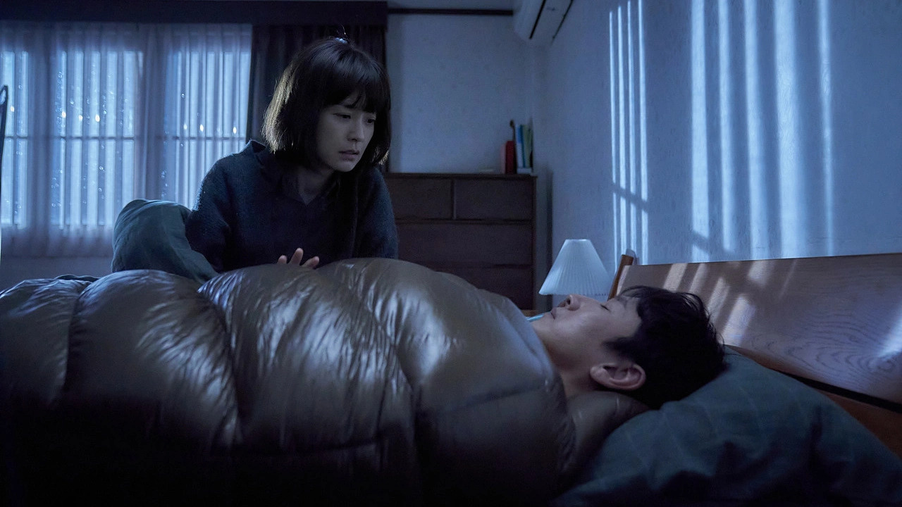 A woman leaning over a sleeping man inside a sleeping bag in Sleep.