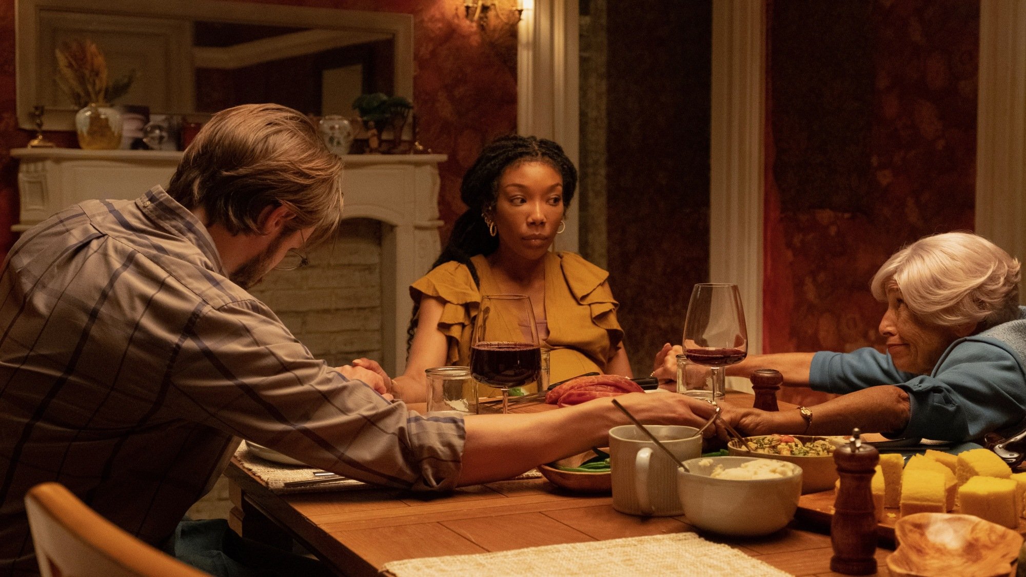 Brandy Norwood sitting at a table and holding hands with a bearded man and an elderly woman in The Front Room.