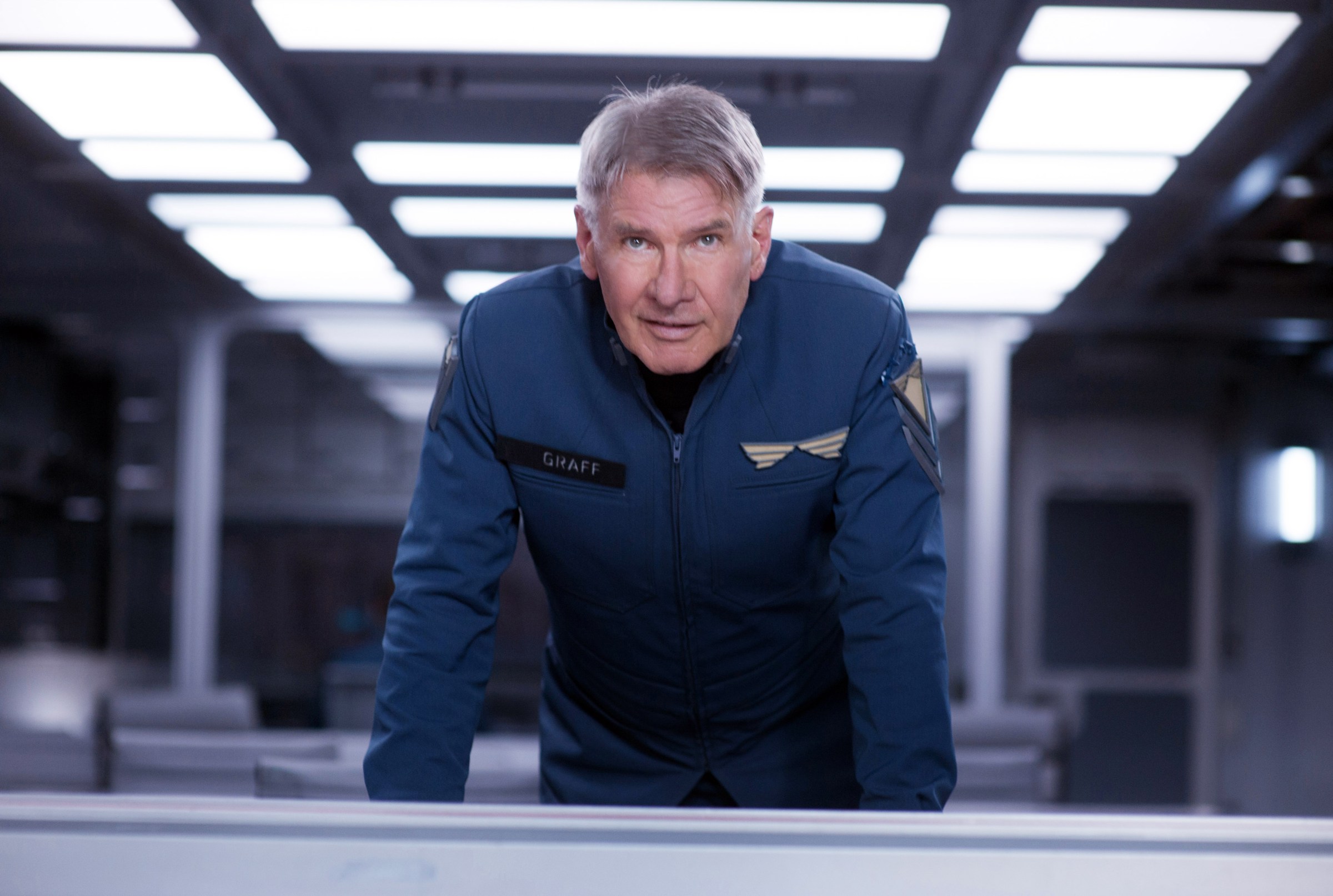 Harrison Ford in a futuristic space uniform leaning over a table in Ender’s Game