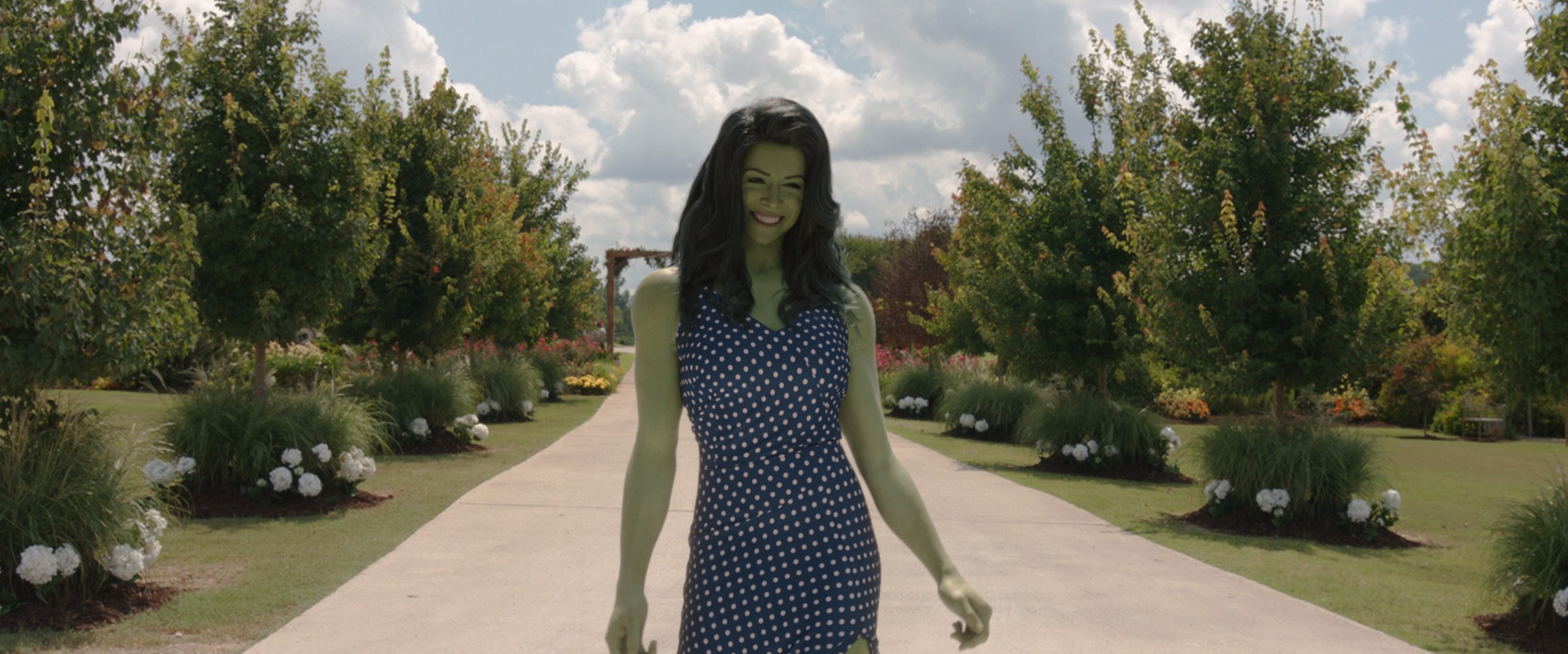 She-Hulk walks down a dirt path in a blue dress with white polka dots