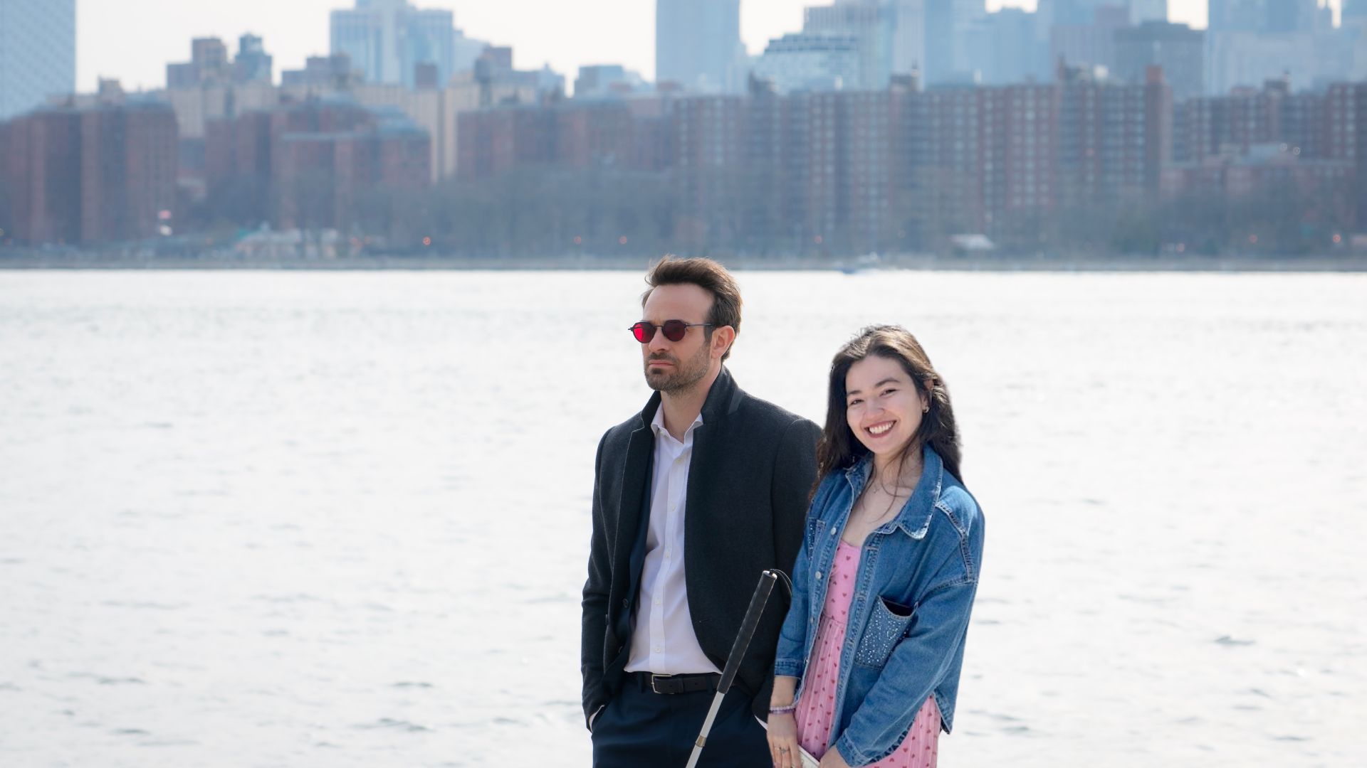 An edited image of Matt Murdock from Daredevil: Born Again and a woman with long dark hair wearing a pink dress and a jean jacket