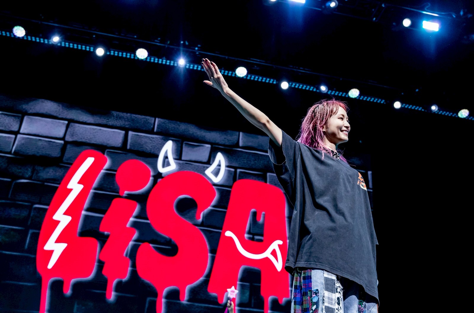 J-pop musician LiSA, on stage with a huge red sign featuring her name — with little devil horns on the “S” — in the background